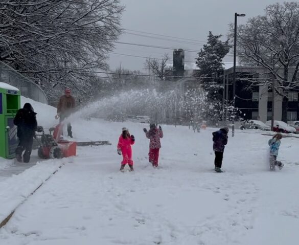 Children play under a spray of snow from a snowblower.